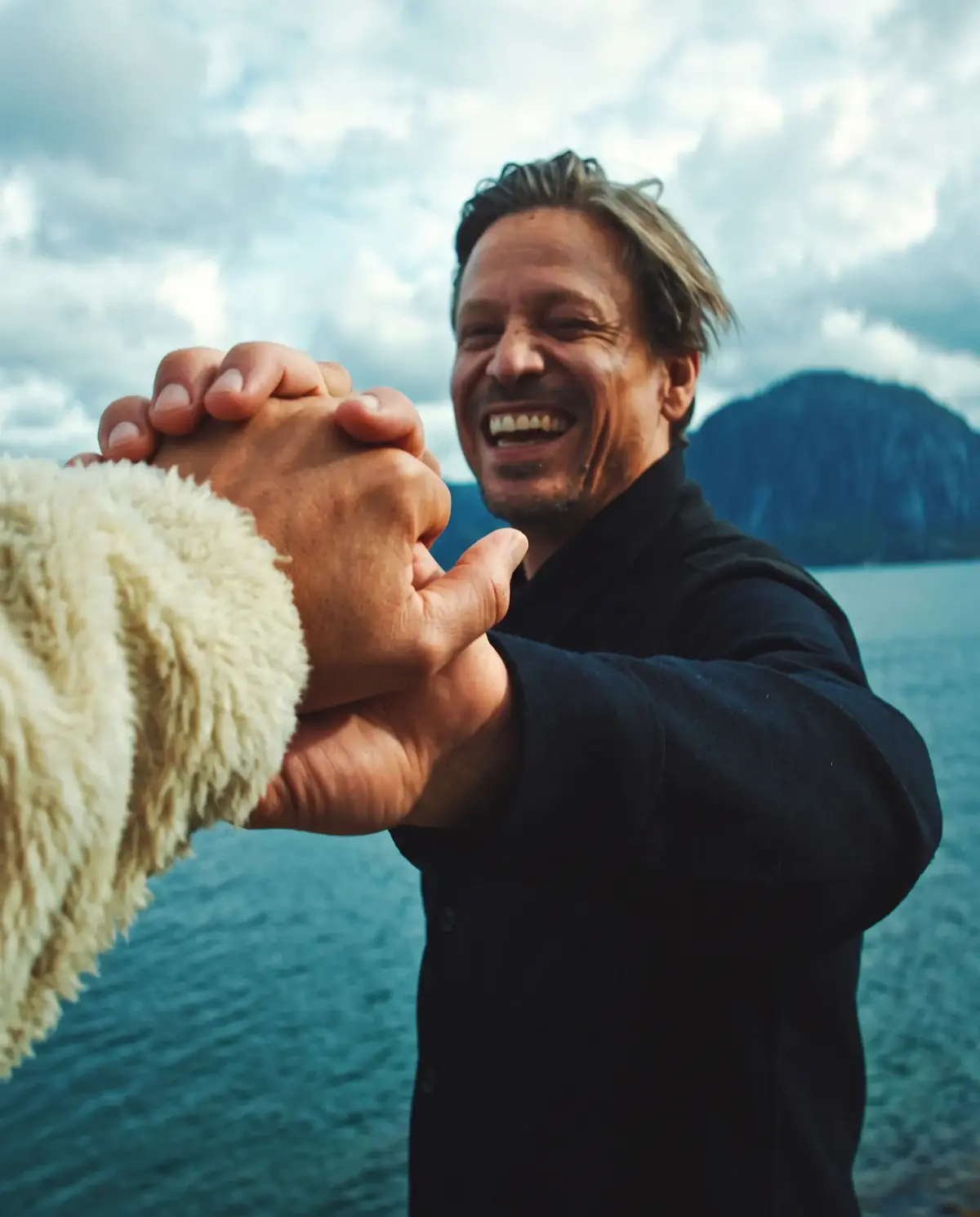 A man smiling while clasping another person’s hand outdoors